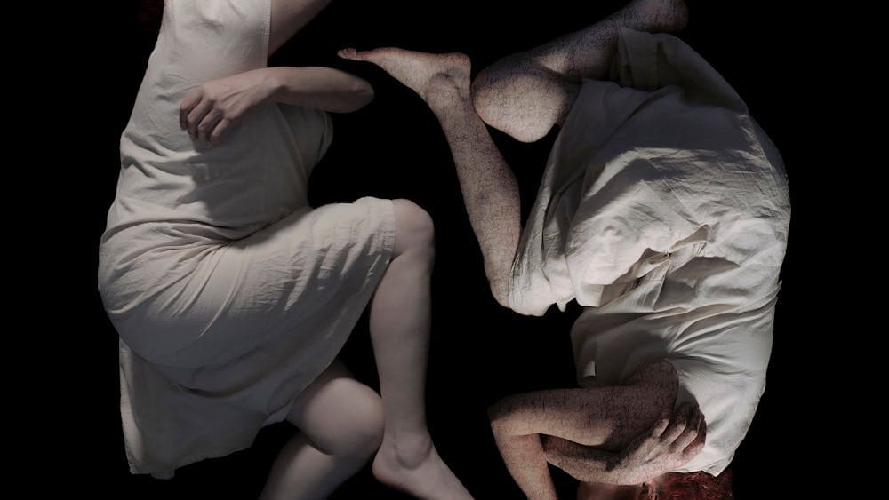 A mirrored image of a woman facing the other in a crouched position appearing troubled or in pain