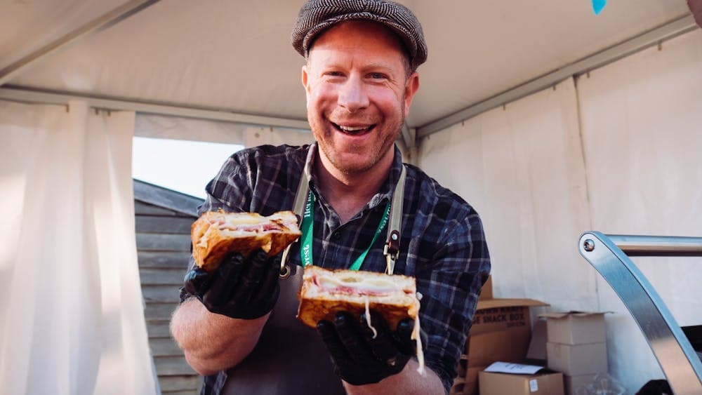 Tim Bone holding up two toasted sandwiches to camera