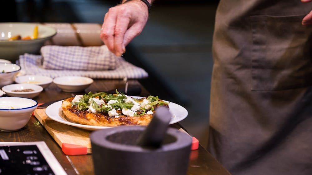 Close up of a hand sprinkling herbs on pizza
