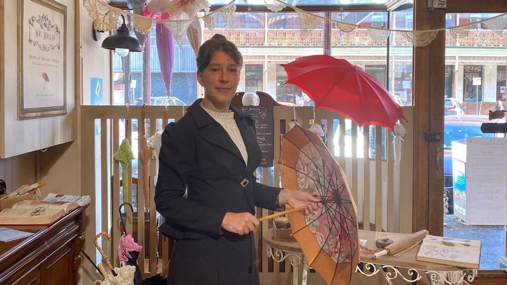 An image of Mrs Muller standing inside her recreated umbrella shop, holding an antique umbrella.