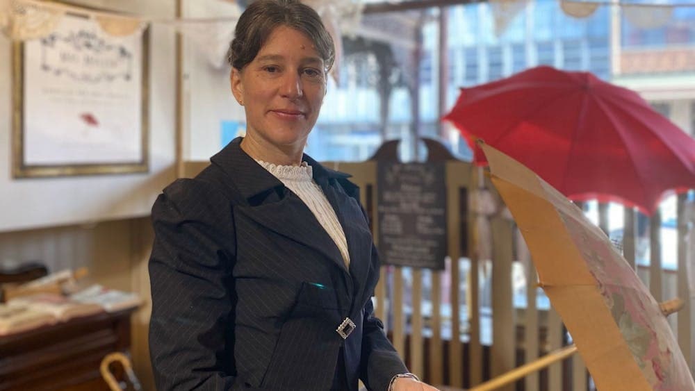 An image of Mrs Muller standing inside her recreated umbrella shop, holding an antique umbrella.