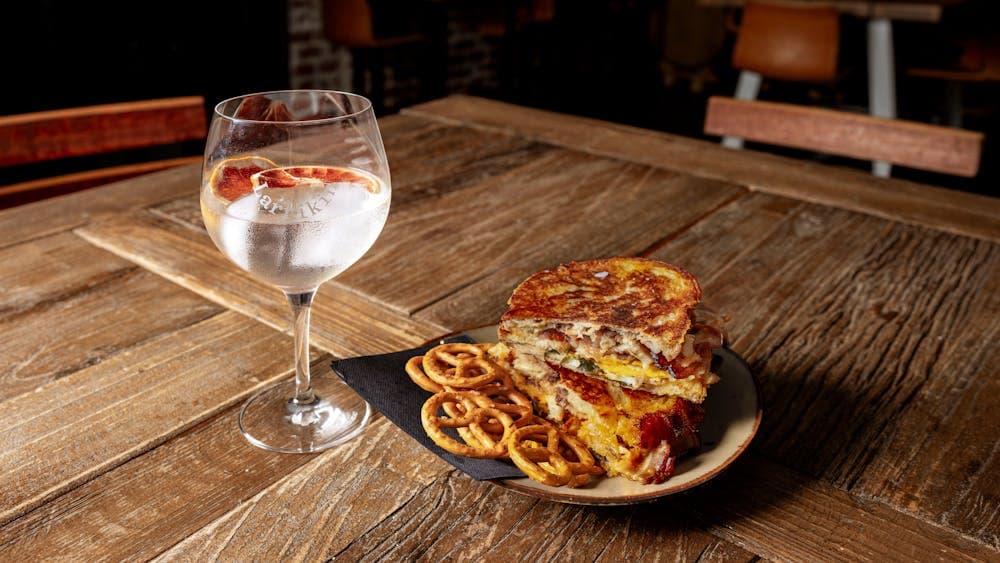 A glass of ice cold gin and tonic next to a gourmet toasted sadnwhich