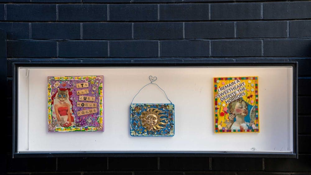 Three mixed media artworks placed in a white box on a black brick wall.