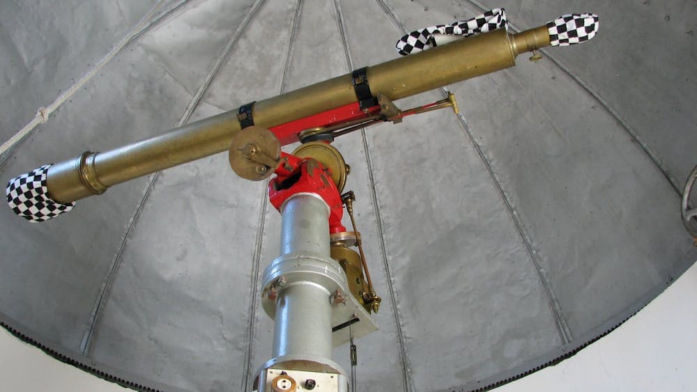 Jelbart 5" scope sits upon an equatorial mount with  black and white dust covers over the lenses.