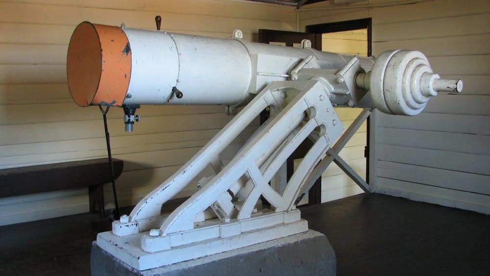White Reflector telescope sits upon equatorial mount. Has orange cover on end.