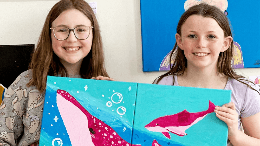 Friends showing a canvas painting of whales that they have painted together