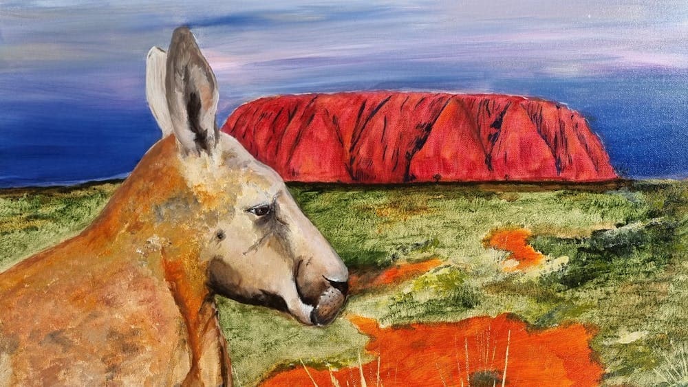 Close up painting of a kangaroo with Uluru in the background in vibrant red and a blue sky.