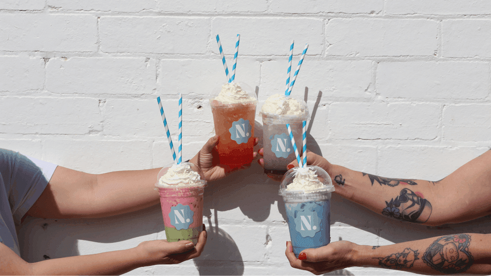 four colourful beverages being held against a white wall