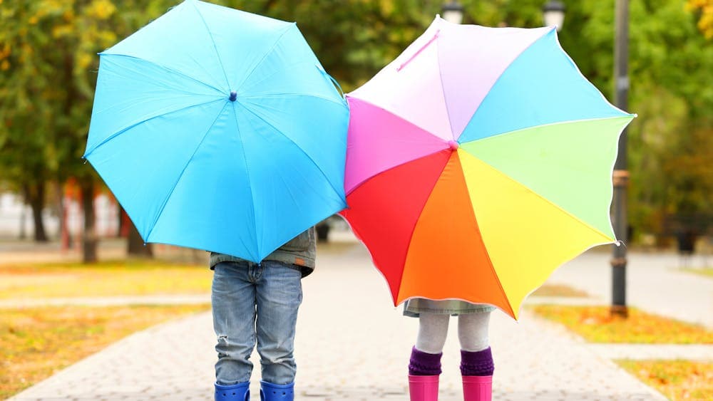 Two children holding umbrellas, one blue and one multi-coloured