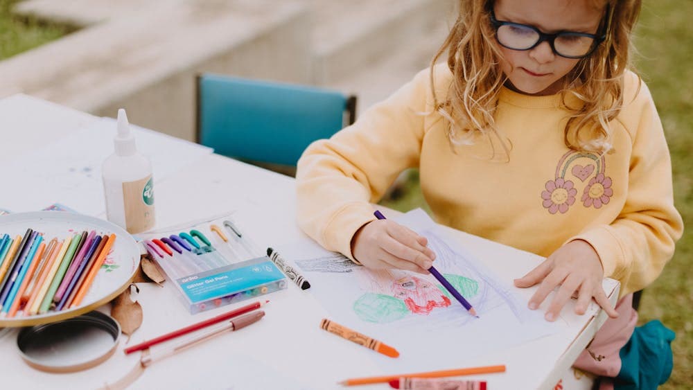 A young girl sits at a table colouring in a drawing on paper