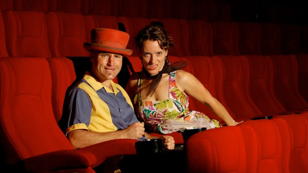 a man and a woman sitting next to each other looking into the camera and biting their lips