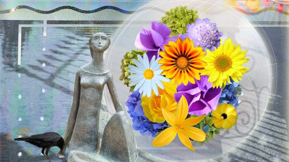 a stone sculpture of a person looking up next to a variety of yellow, purple, white and blue flowers