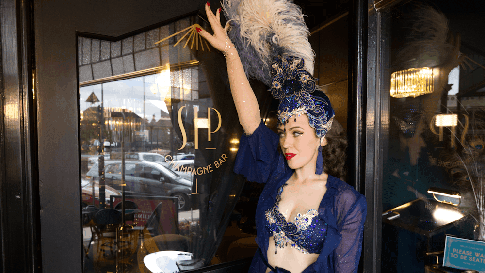 Burlesque dancer standing at Sip Champagne Bar door raising their hand