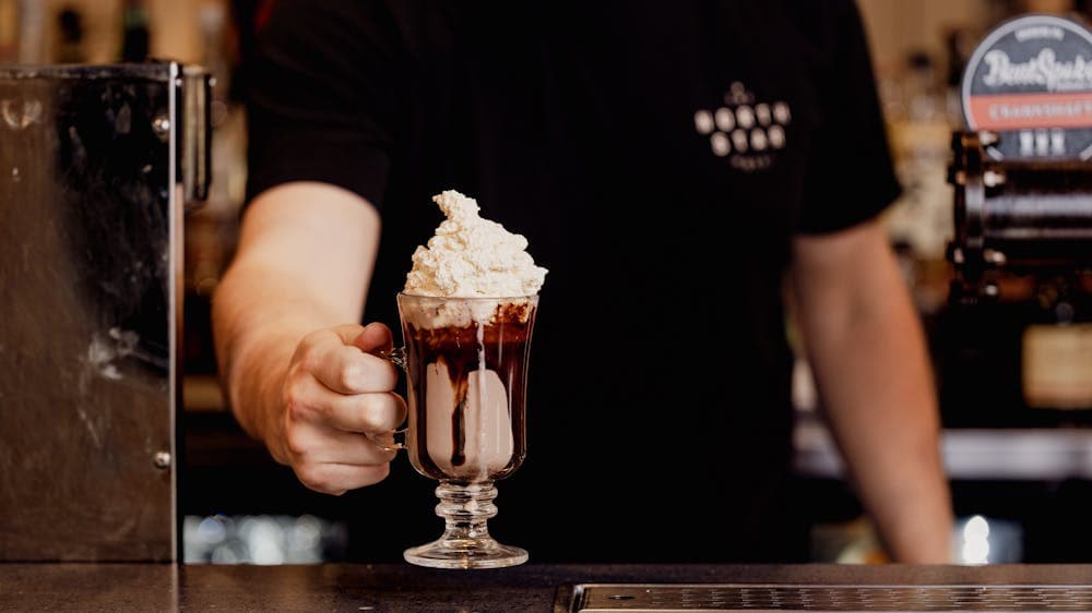 brown chocolate drink ina glass mug with chocolate sauce on the side and whipped cream on top