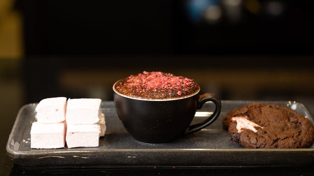 hot chocolate in a black mug on a steel tray with a cookie and marshmallows beside it