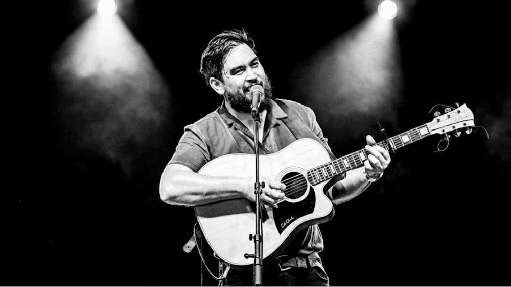 Black and white image of musician, Grim Fawkner, on stage with a guitar and microphone.