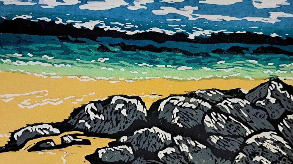 Grey rocks, yellow sand and the dark blue sea and cloudy sky