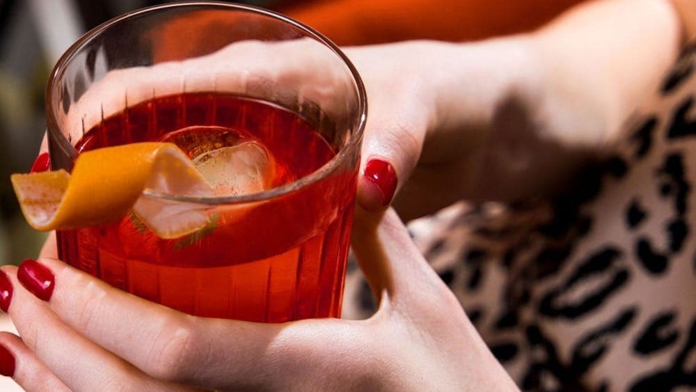 A woman's hands with red painted nails holding a red cocktail