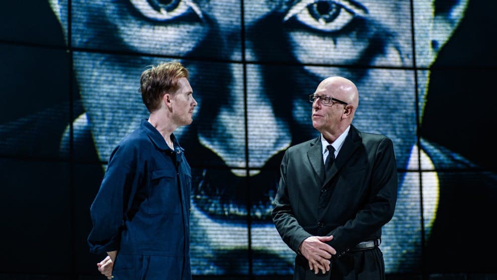 Two men talking with Big Brother on a screen behind watching