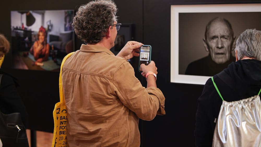 A man in a brown shirt uses his mobile phone to photograph a portrait exhibition.