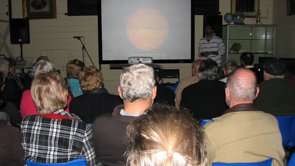 Back of peoples heads watching a screen with a picture of that sun as a presenter is speaking