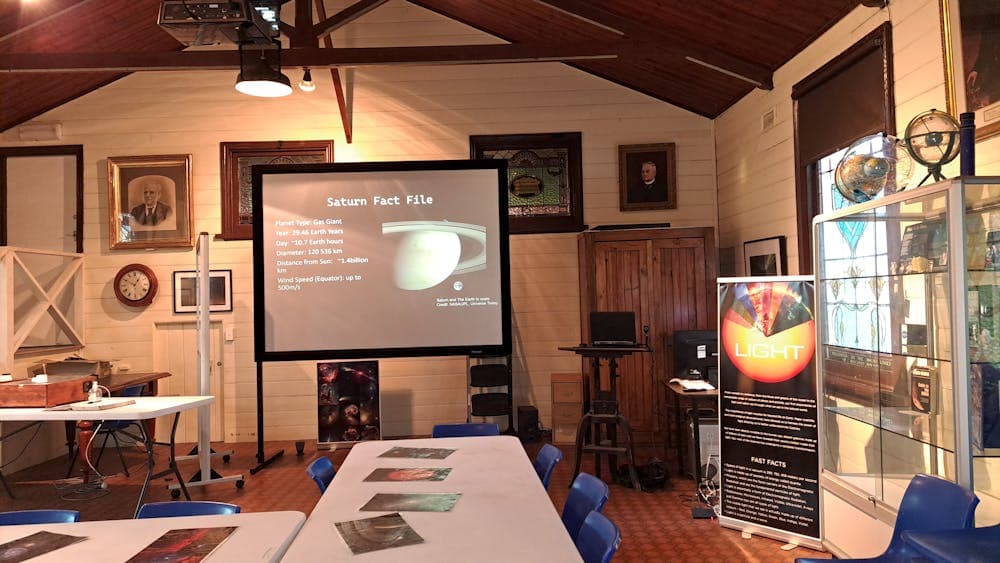 Room with picture of saturn on a screen and tables with laminated pictures of space laid on top.