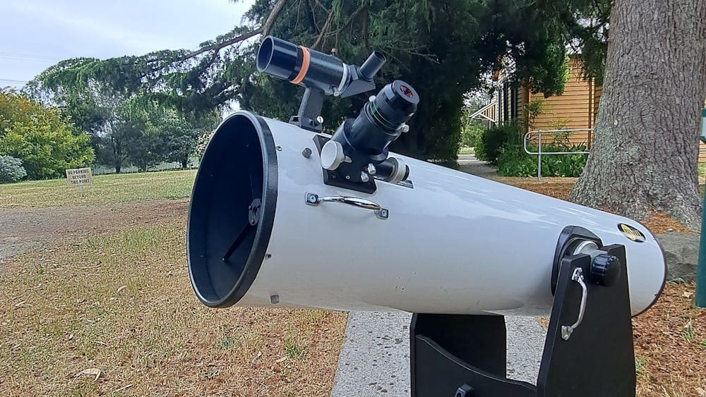 White Dobsonioan telescope with eyepiece, finder scope, handle and stand sits on footpath .