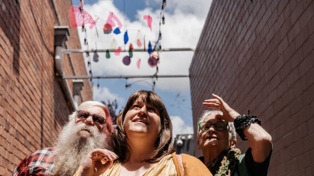 3 people look up, interested in th hanging artworks in a laneway, cloudy blue sky in the background.