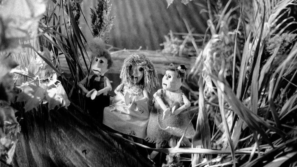 Black and white live action puppetry scene with three puppets in a forest