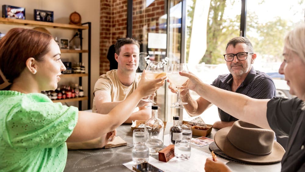 four people sitting around a table, holding up their glass to cheers