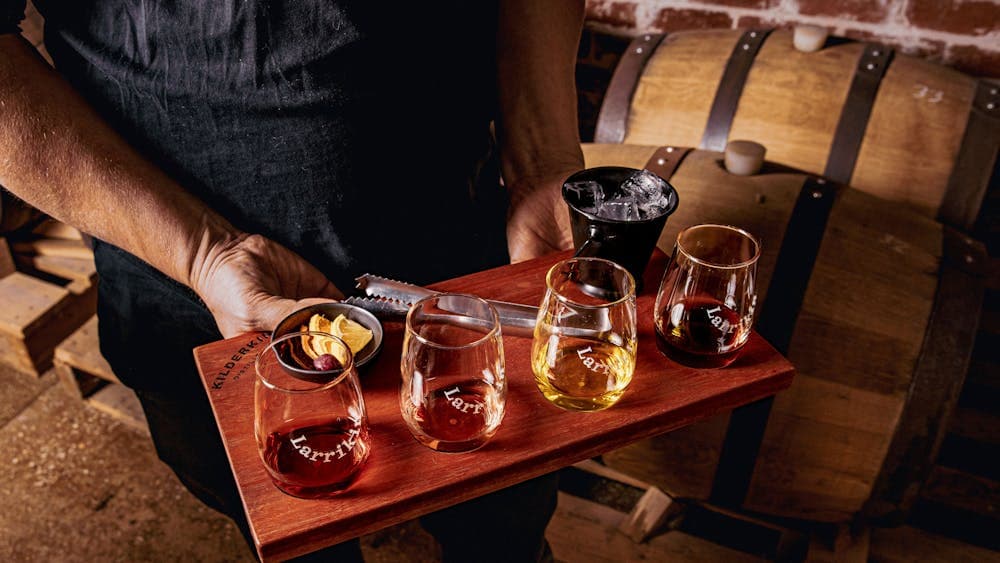 four glasses of spirits sitting on a serving board being held by the waiter