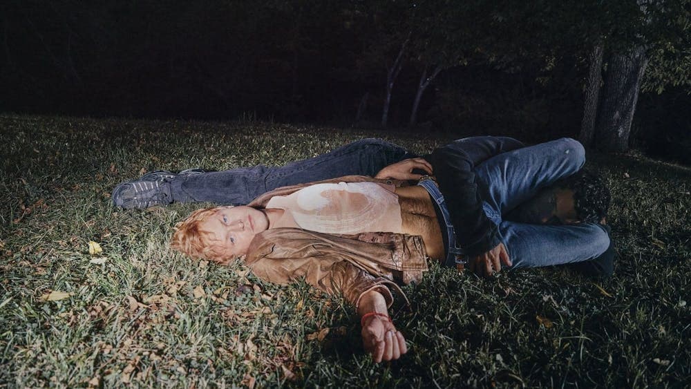 Perfume Genius laying in grass at night, another man is entangled with him.