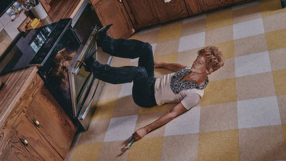 Perfume Genius is laying on his back in a kitchen and wearing high-heeled boots