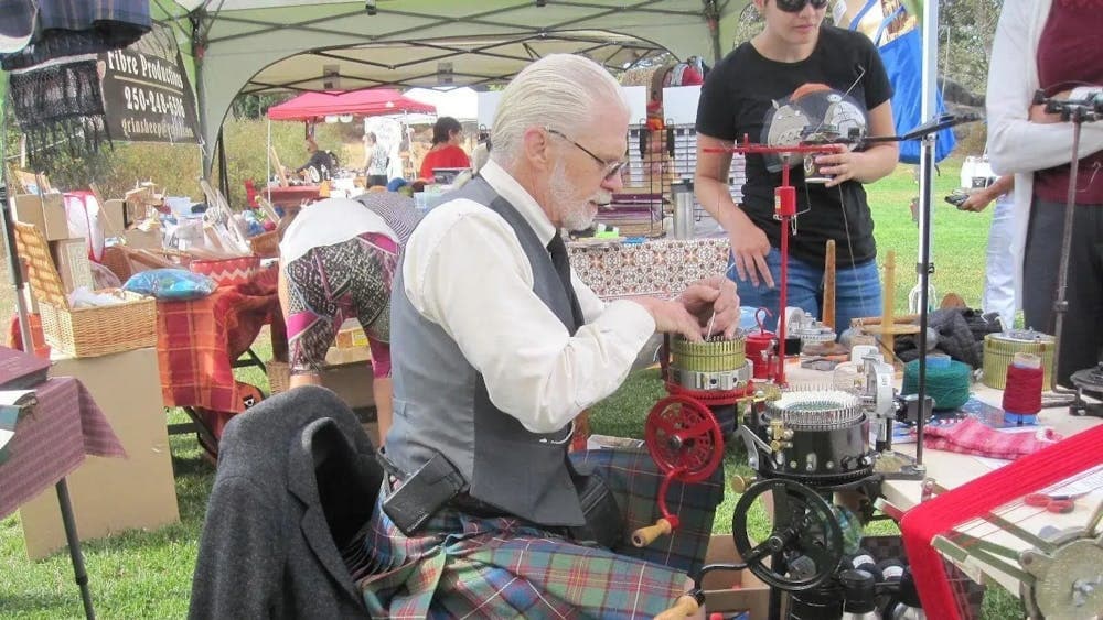 Man wearing kilt, vest and shirt seated at table operating a Crank Sock Machine