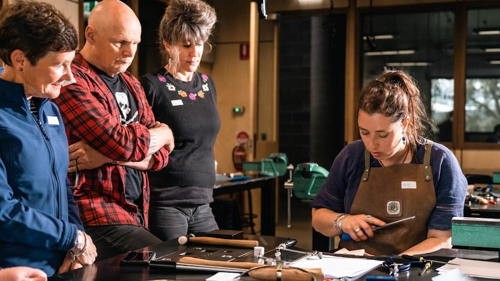 Woman at demonstrating at work bench with three people standing and looking on