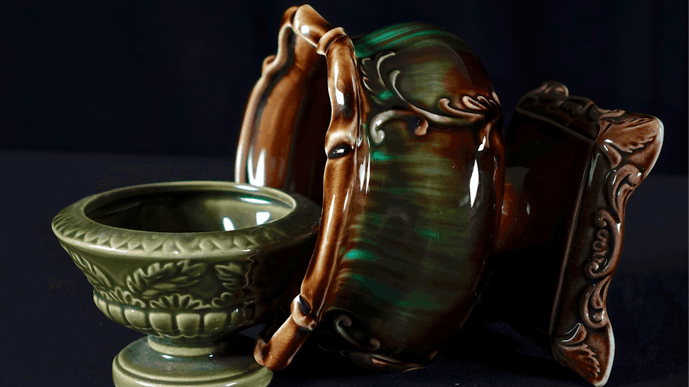One small green ceramic vase upright and a larger laid on its side with a black background.