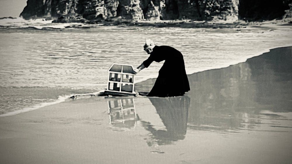 Woman in a black dress dragging a miniature house our of the ocean