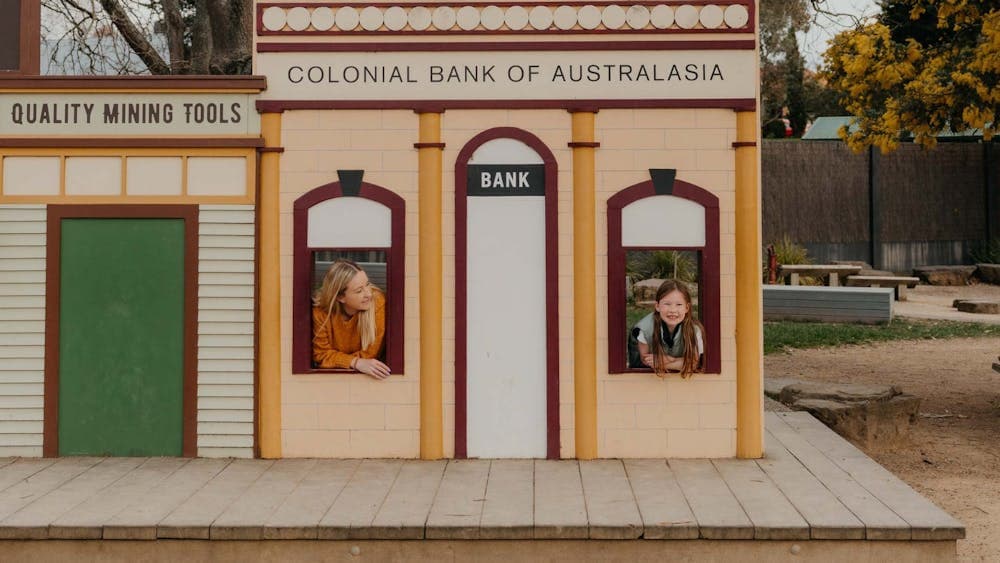 Mother and daughter peering outside windows in miniature building at Sovereign Hill playground