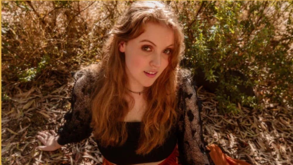 A young woman with red hair sitting on the ground looking up at the camera