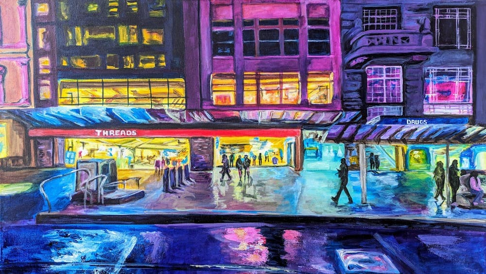 Night scene of a city street with brightly lit buildings, lights reflecting off the road.