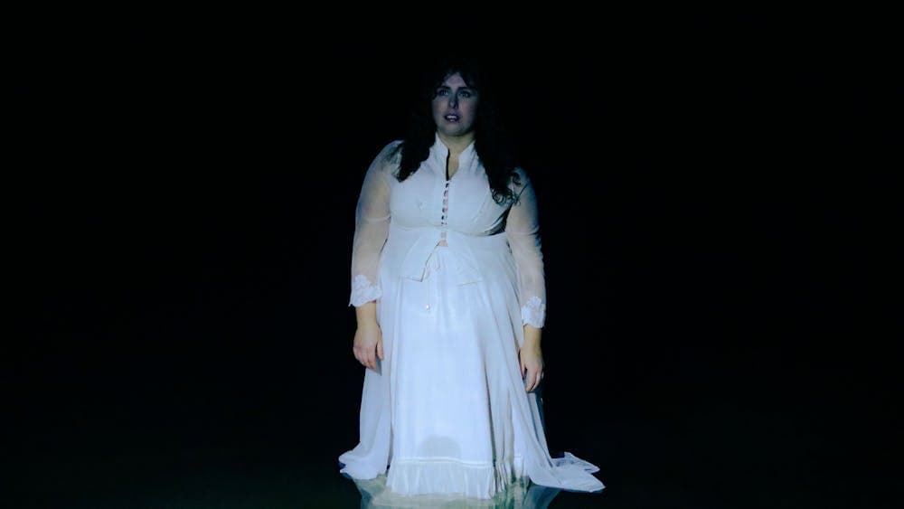 A dark photo of a woman dressed in white standing in water