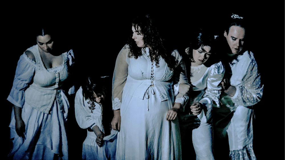 Five women, dressed in white, looking down into the water