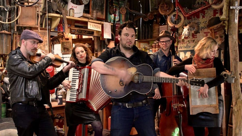 Five musicians each holding a different instrument including guitar, piano accordian and fiddle.