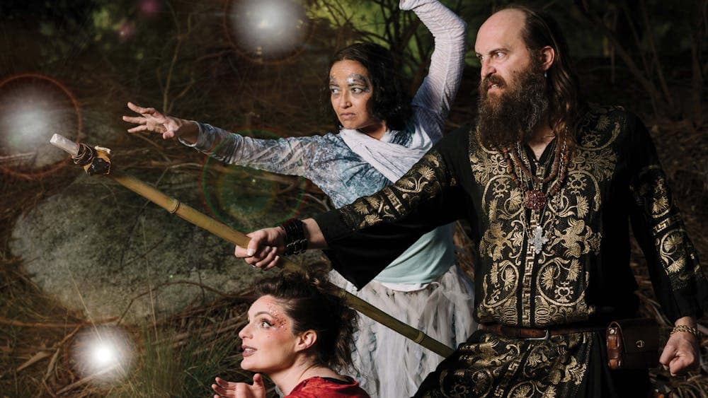 Three magical characters in intricate clothing. One holds a staff with a crystal at its tip.