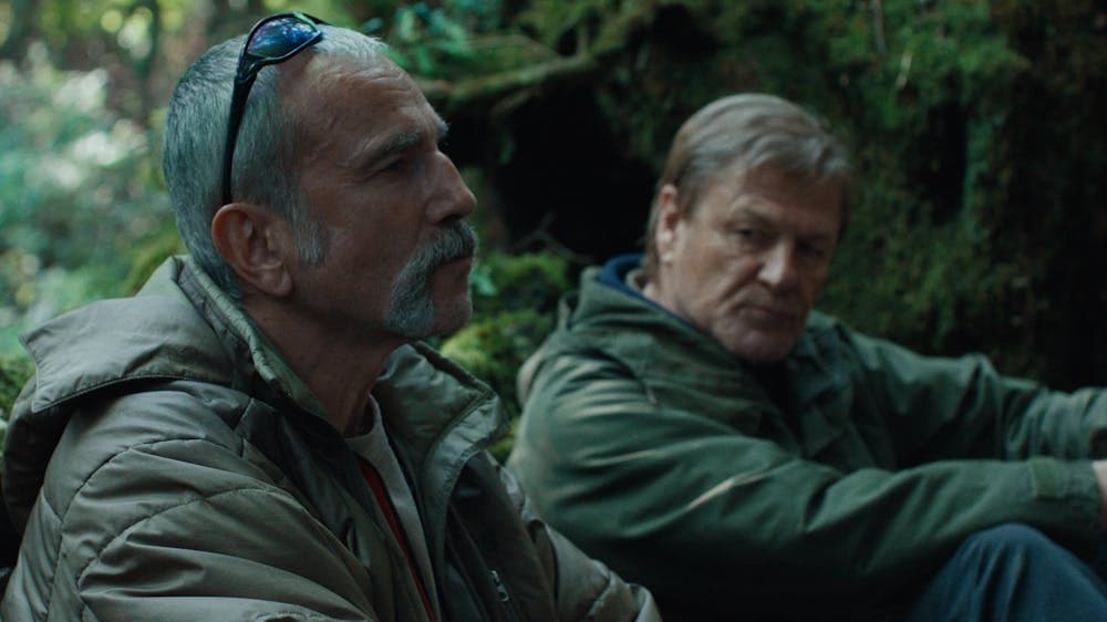 Two men sit on forest floor