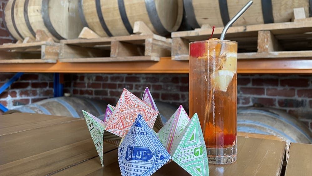 Image shows glass with cocktail alongside chatterbox in front of barrels