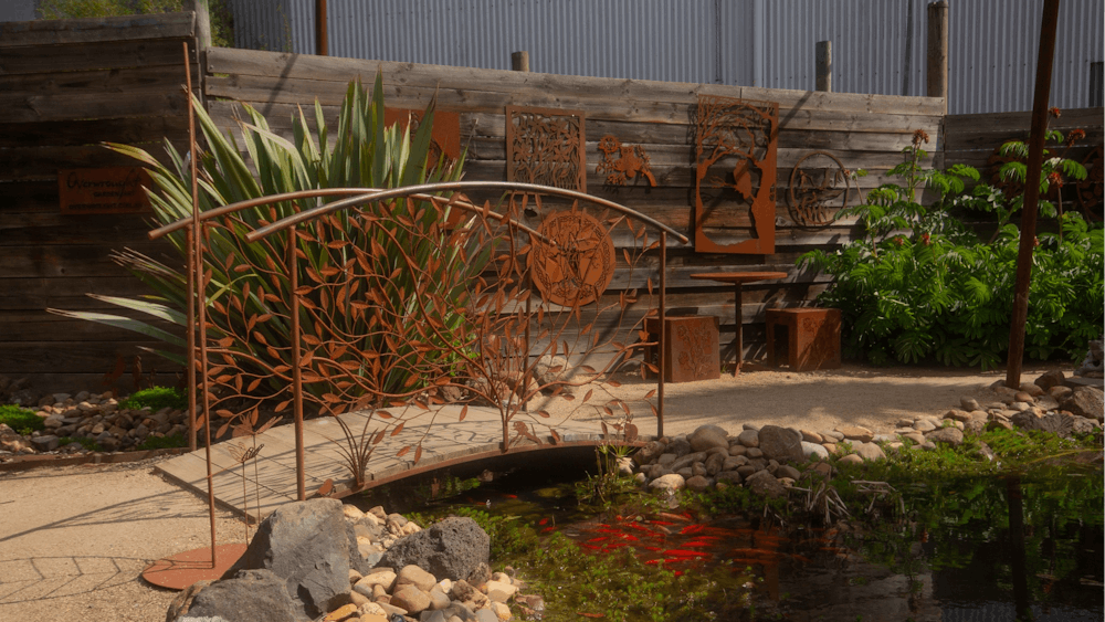 In the forground is a pond brimming with fish behind is an ornate metal bridge and range of wallart.