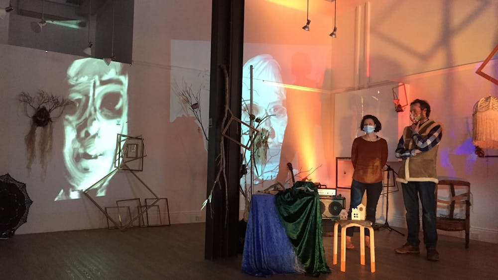 Two performers stanging in the space with digital projections on the wall.