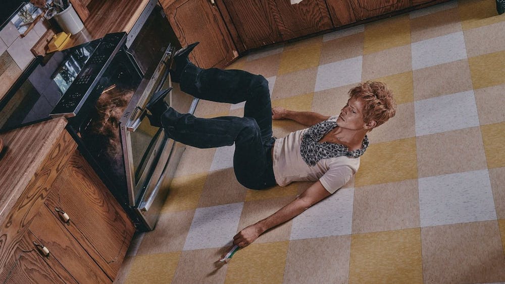 Perfume Genius is laying on his back in a kitchen and wearing high-heeled boots