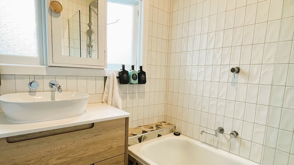 Bathroom with shower over bath, opening window, vanity and luxurious soaps.